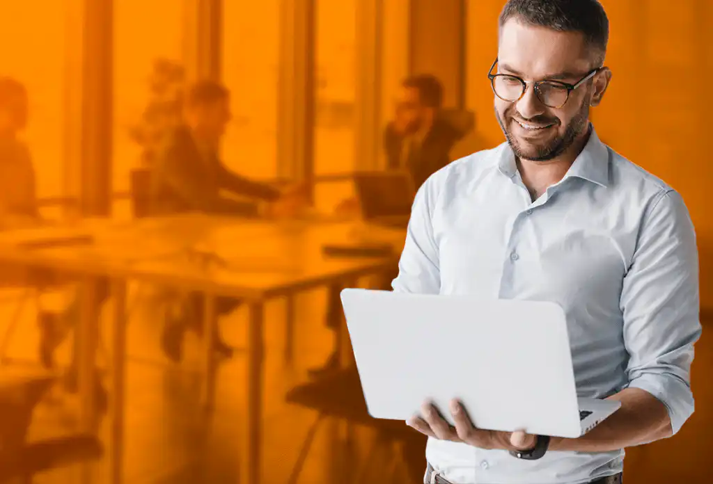 A Man Smiling In Front Of A Laptop With Group Of People Having A Meeting On His Background For SEO Training Pricing Options