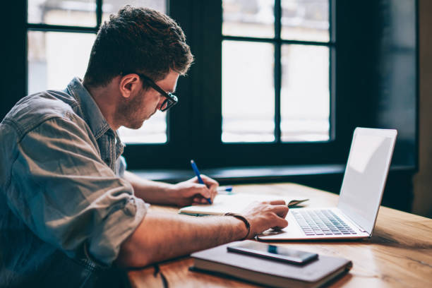 A person writing in a notebook at a table with a laptop representing SEO training for copywriters